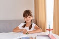 Portrait of of dark haired little girl drawing something in album sitting at the table near window, cute kid with braids looking Royalty Free Stock Photo