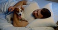 A portrait of a dark-haired man with a middle-aged beard, lying in a white bed with his small dog, playing with it Royalty Free Stock Photo