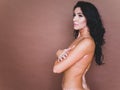 Portrait of naked woman with vitiligo covers her breast on brown background