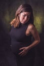 Dark-haired pregnant woman in a black tight dress holding her big gestation belly with her hands Royalty Free Stock Photo