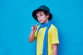 Portrait of defiant boy in yellow t-shirt, scarf and hat doing, on blue background. Copy space