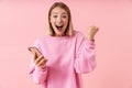 Portrait of delighted blonde woman screaming and holding smartphone