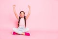 Portrait of delighted child raise fists scream shout yeah sitting dressed white pants trousers over pink