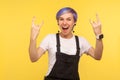 Portrait of delighted funky hipster woman showing rock and roll gesture, crazy punk sign. yellow background, studio shot