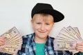 A portrait of delighted little stylish boy in black cap holding money in his hands. A happy child male holding cash isolated over