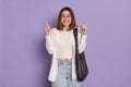Portrait of delighted satisfied woman with black bag wearing white shirt and jeans, looking at camera with toothy smile, pointing Royalty Free Stock Photo