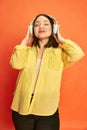 Portrait of delightful, beautiful, young, asian girl listening to music in headphones against orange studio background Royalty Free Stock Photo