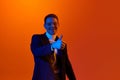 Portrait of delightful happy young man in jacket and glasses posing with positive finger gesture against orange studio