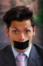 Portrait of a desperate businessman, with a black tape in his mouth, in a blurred background