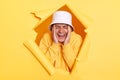 Portrait of desperate depressed man wearing hoodie and panama posing in hole in yellow paper wall, keeps hands on head, screaming Royalty Free Stock Photo