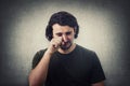 Portrait of desperate young man crying and wiping the tears with his hand isolated on grey wall background. Dissatisfied and