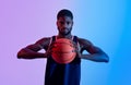 Portrait of determined young black basketballer holding ball and looking at camera in neon light