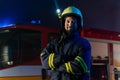 Portrait of dirty firefighter man on duty with fire truck in background at night, smiling.