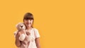 Portrait of disabled girl with Down syndrome smiling at camera, holding her teddy bear while posing isolated over yellow Royalty Free Stock Photo