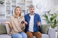 Portrait of disappointed cheated family, man and woman mature couple sitting sad on sofa and looking at camera, using Royalty Free Stock Photo