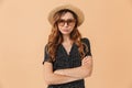 Portrait of disappointed woman 20s wearing straw hat and sunglasses standing with arms crossed, isolated over beige background