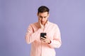 Portrait of disappointedyoung man holding phone with doubtful and skeptical expression on pink isolated background. Royalty Free Stock Photo