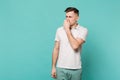 Portrait of disconcerted young man in casual clothes looking aside, covering nose with hand isolated on blue turquoise