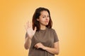 Portrait of a discontented young Caucasian woman showing a hand gesture of stop and ban. Yellow background. Human emotions, the Royalty Free Stock Photo