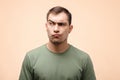 Portrait of disgruntled man with pouting lips in green T-shirt on beige background