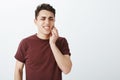 Portrait of displeased suffering young male model in red t-shirt, frowning and clenching fists, touching jaw while