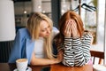 Portrait of displeased young woman and best female friend trying to comfort and cheer up sitting together in cafe by Royalty Free Stock Photo