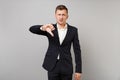 Portrait of dissatisfied young business man in classic black suit, shirt showing thumb down isolated on grey wall Royalty Free Stock Photo