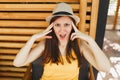 Portrait of dissatisfied young woman in straw summer hat, yellow shirt put hands on head on wooden background in