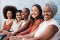 Portrait, diversity and a group of happy businesswomen sitting in a line as coworkers against a wall outside in the city