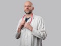 Portrait of a doctor on light color background. Male in 40s with grey beard in clinic uniform with stethoscope. Open friendly face