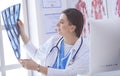 Portrait of doctor sitting in office holding xray image, working on computer