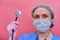 Portrait of a doctor woman in a medical cap with a stethoscope, closeup. Nurse in a blue uniform and a protective mask on a pink