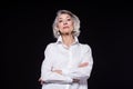 Portrait of a domineering, arrogant mature woman looking down and standing with her arms crossed isolated on a black Royalty Free Stock Photo