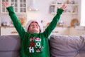 Portrait dreaming boy with closed eyes in Santa hat and Christmas costume sitting at home hands up. New Year Holidays