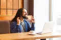 Portrait of dreaming handsome young adult man freelancer in casual style sitting in cafe with laptop, showing crossed finger with