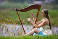 Portrait of dreaming sensual female harpist in light dress playing music outdoor in park