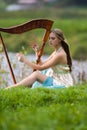Portrait of Dreaming Sensual Female Harpist in Light Dress Playing Music Outdoor in Park