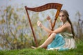 Portrait of Dreaming Sensual Female Harpist in Light Dress Playing Music Outdoor in Park