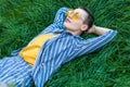 Portrait of dreamy beautiful young woman with short hair in casual blue striped suit, yellow shirt and glasses lying down on green