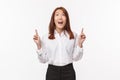 Portrait of dreamy japanese young office lady in white shirt, looking and pointing up amused, smiling wondered checking Royalty Free Stock Photo