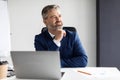 Portrait Of Dreamy Mature Businessman Sitting At Desk With Laptop In Office Royalty Free Stock Photo