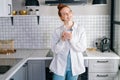 Portrait of dreamy redhead woman holding cup of hot beverage in hands on morning at kitchen. Royalty Free Stock Photo
