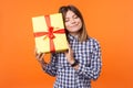 Portrait of dreamy woman with charming smile in casual checkered shirt holding gift box. isolated on orange background