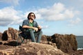 Portrait Of Dreamy Young Man Sitting On Beach Rocks Near Ocean Royalty Free Stock Photo