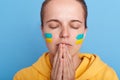 Portrait of eared depressed frightened emotional woman with Ukraine flag on face, praying for stop war between Russia and Ukraine Royalty Free Stock Photo