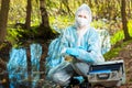 portrait of an ecologist in protective clothing while working, taking water samples from a forest river