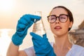 Portrait of ecologist wearing protective gloves and eyeglasses, examines test sample flask of water. Concept of