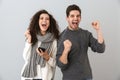 Portrait of ecstatic couple man and woman listening to music with earphones and dancing, isolated over gray background