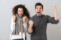 Portrait of ecstatic couple man and woman screaming while clenching fists, isolated over gray background