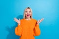 Portrait of ecstatic excited girl with blond hairdo wear knit orange jumper raising palms staring isolated on blue color